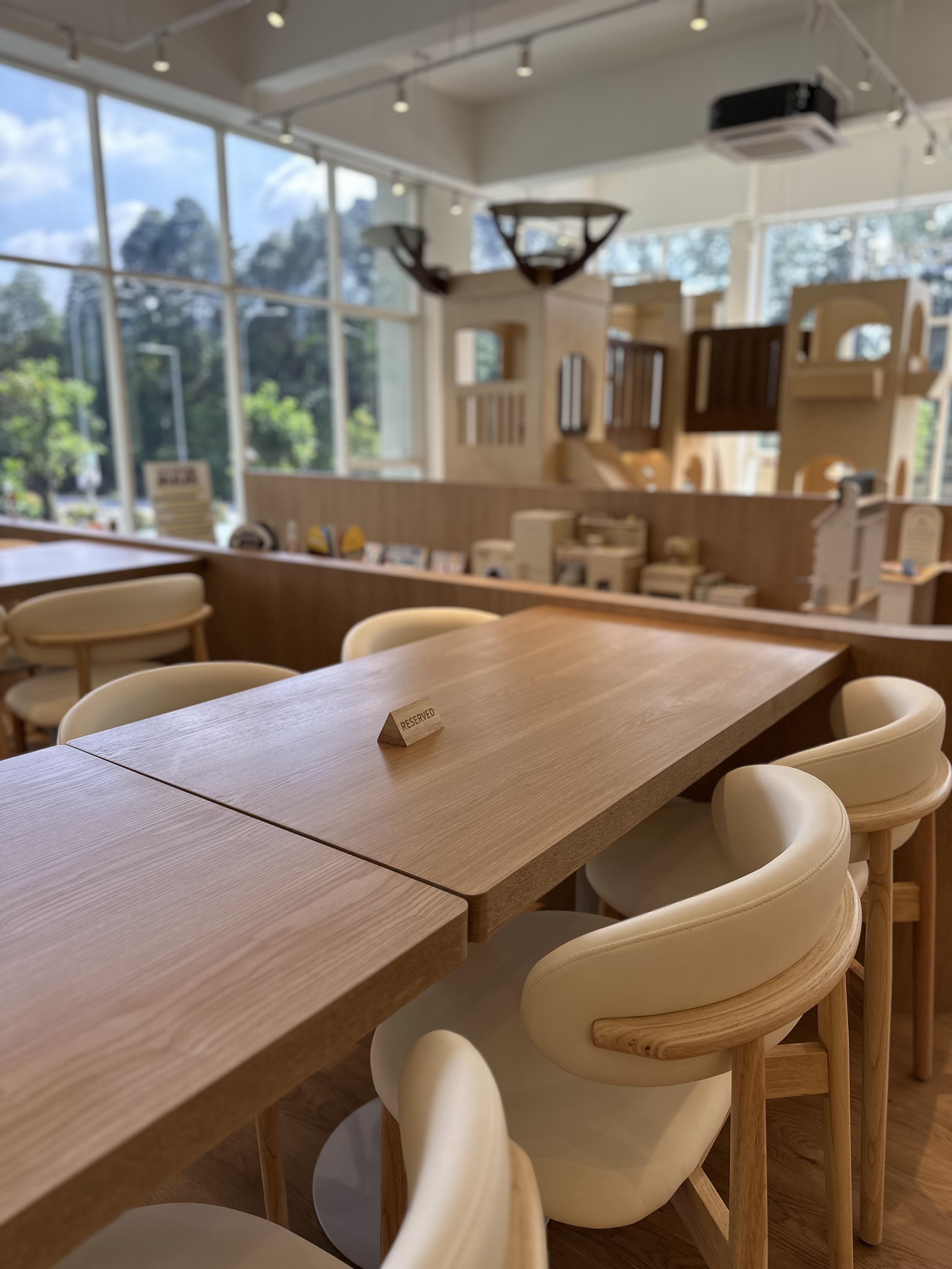 The interior of Naru Play Café — wooden tables, cream chairs, large windows, and the play structure in the background.