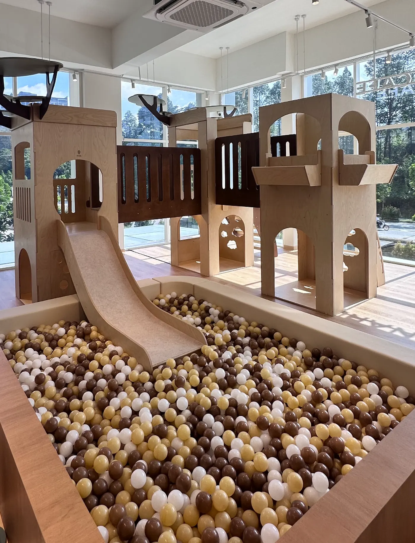 The big kids' play structure at Naru — a multi-level wooden castle with a slide leading into a large ball pit filled with cream, caramel and brown wooden balls.