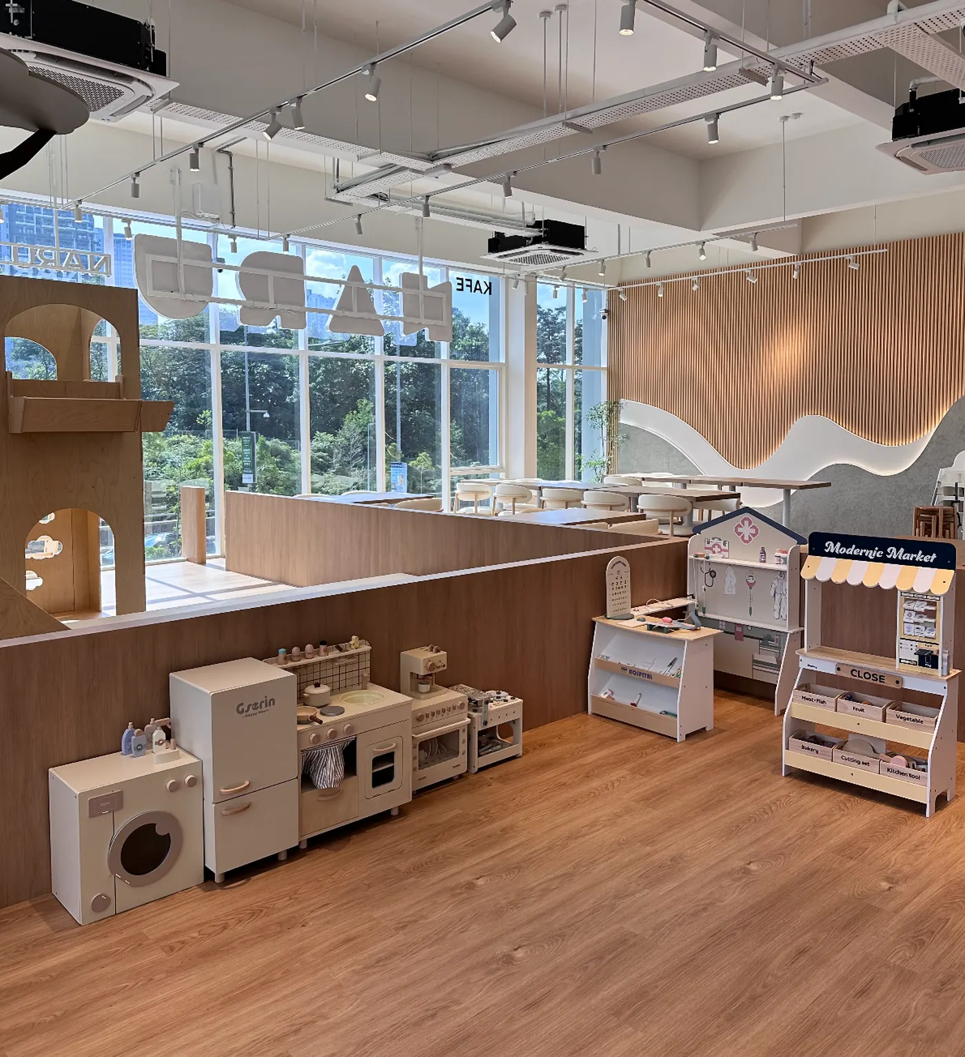 The under-3s area at Naru — wooden pretend-play kitchen, washing machine, mini market stall and a soft play corner, low to the ground and gentle on the senses.